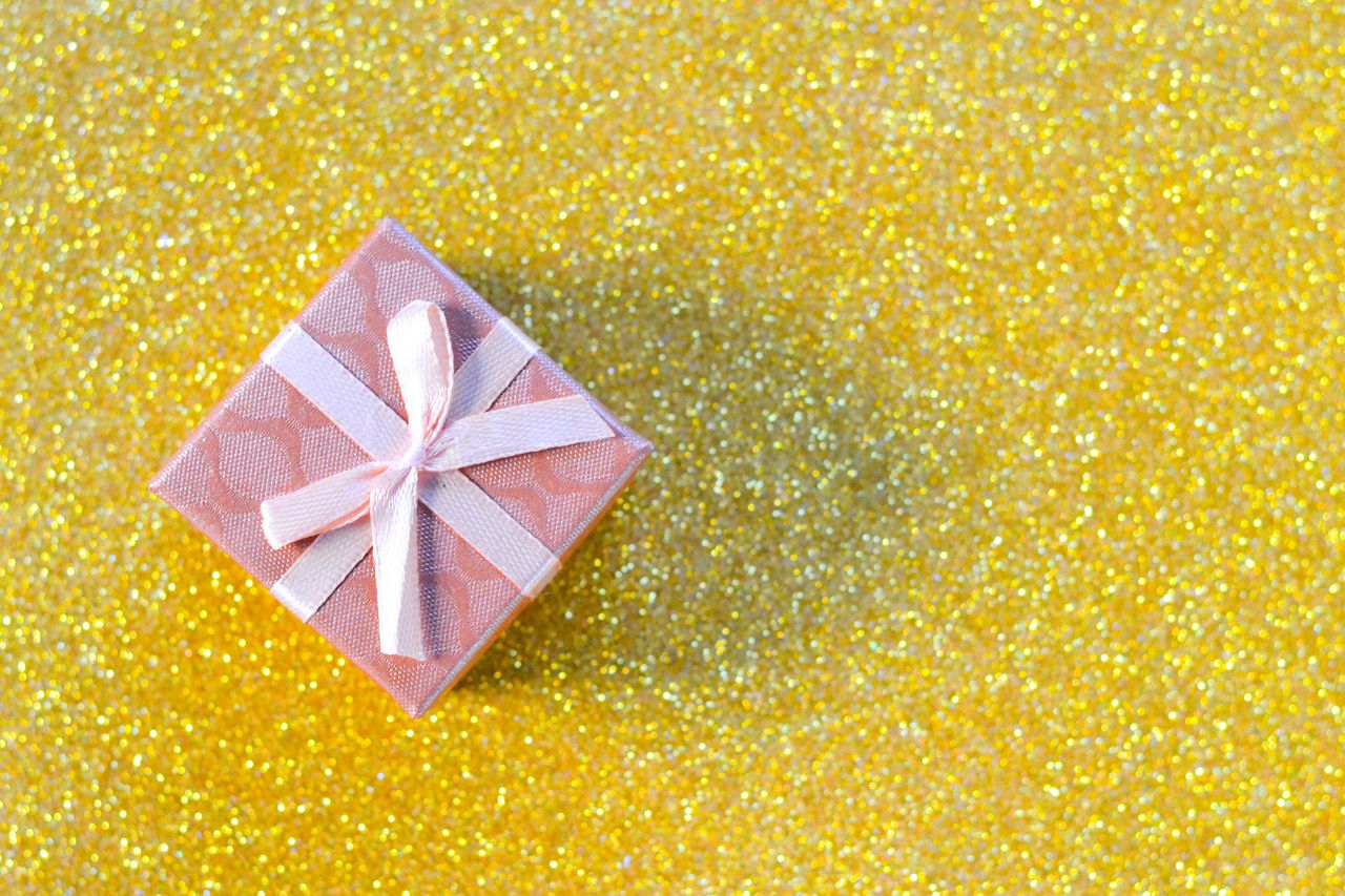 services-03 Beautifully wrapped pink gift box on a sparkling gold glitter background, perfect for celebrations.
