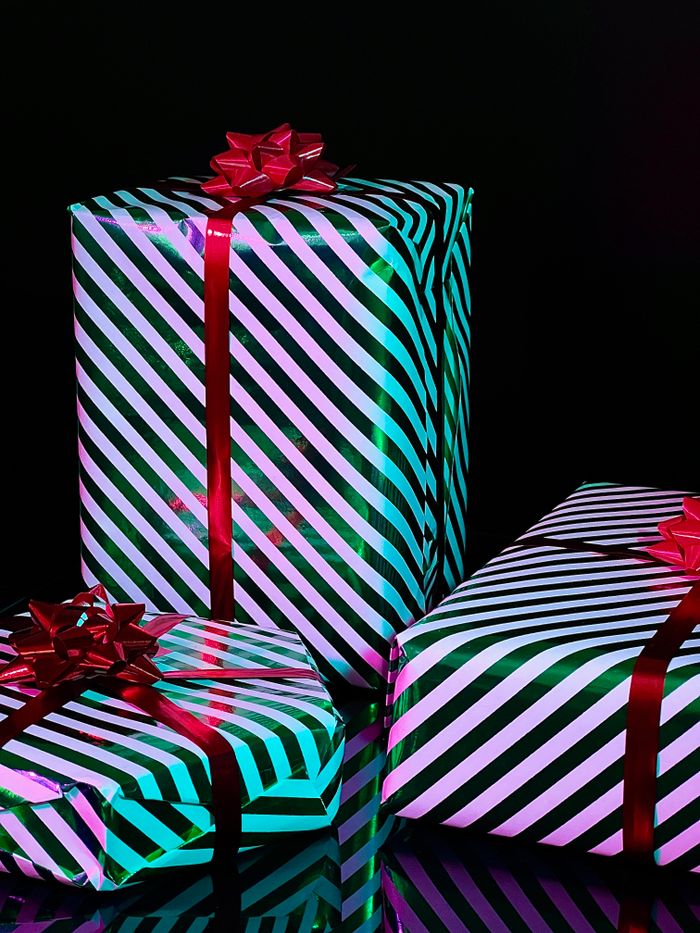 services-04 Vibrant gift boxes wrapped in striped paper with red bows on a black background. Ideal for holiday themes.