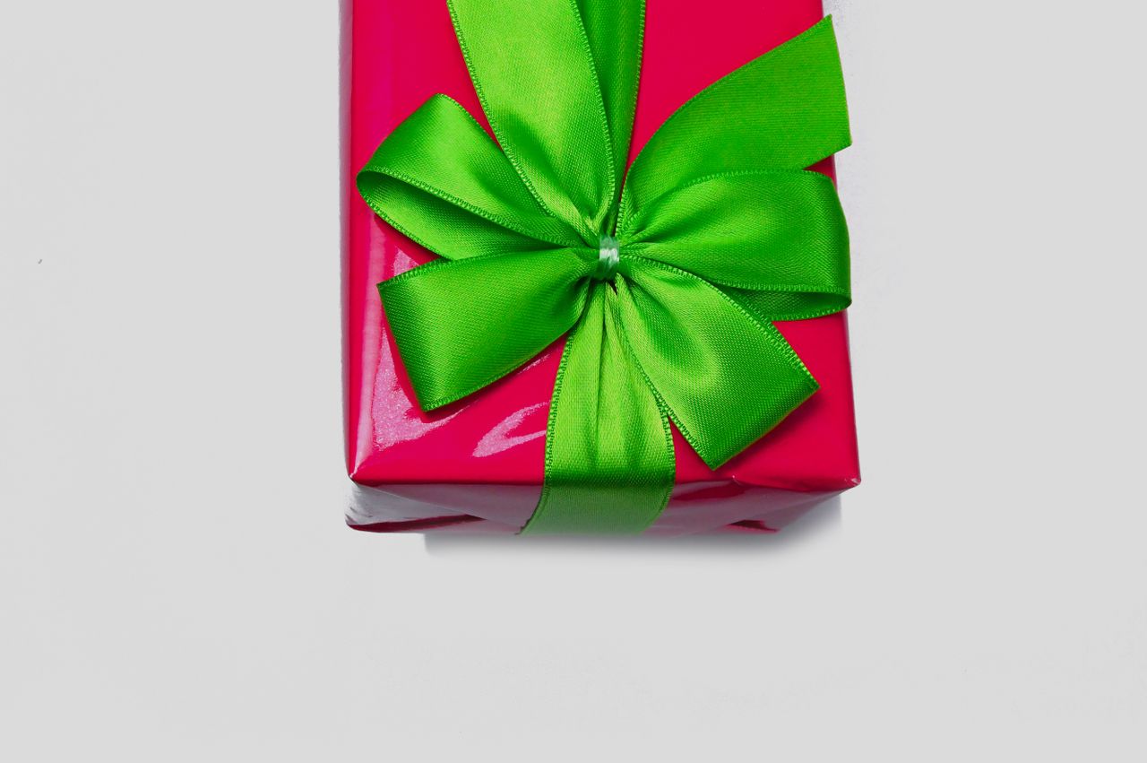 who-we-are A bright red gift wrapped in a glossy paper with an elegant green ribbon bow.