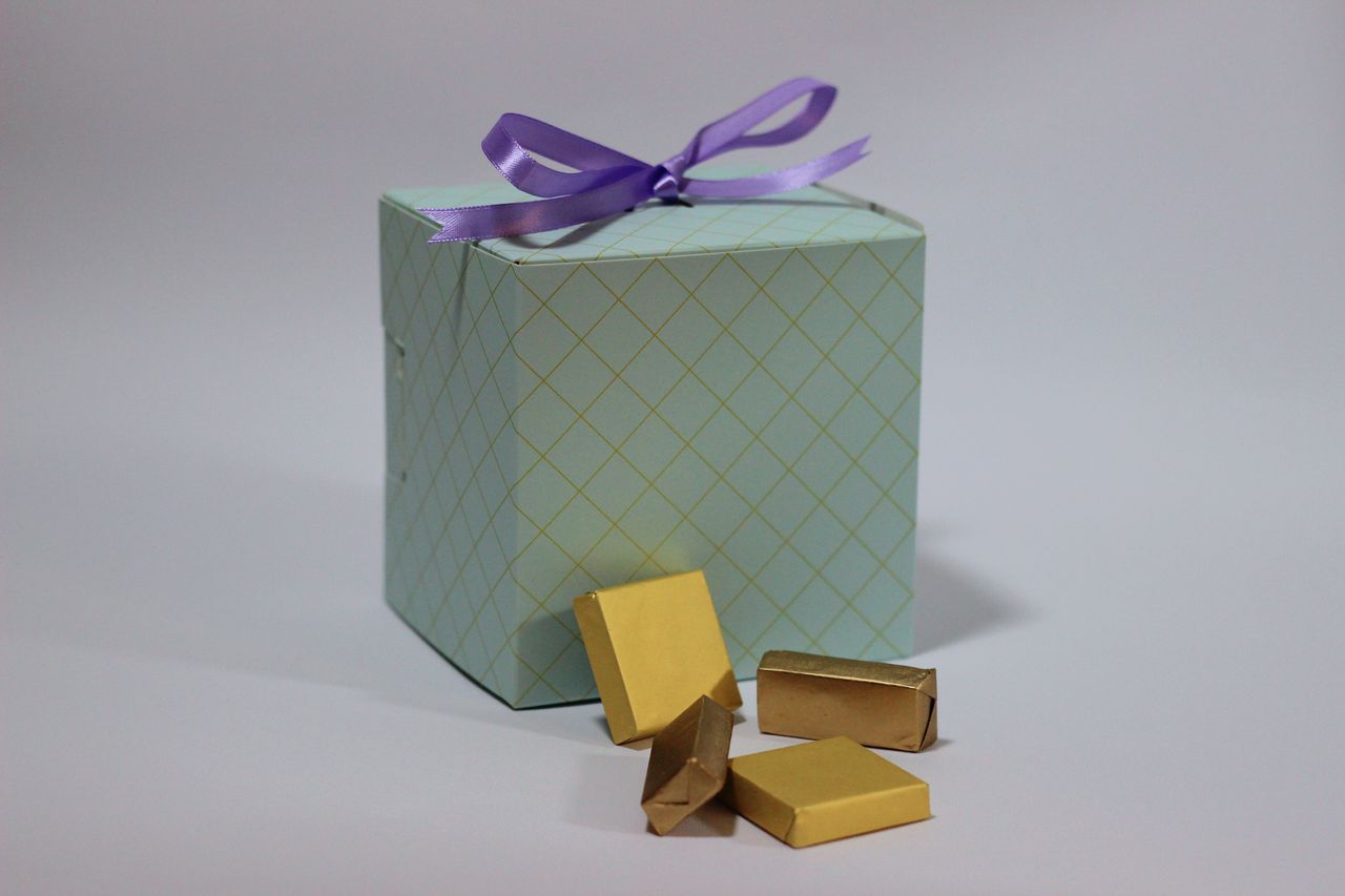 A pastel gift box with a purple ribbon and gold-wrapped chocolates perfect for celebrations.